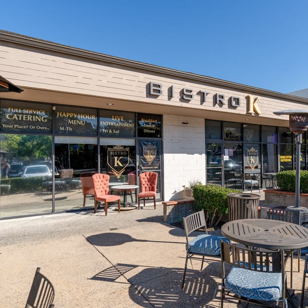 Exterior of The Bistro K, an Italian restaurant, with outdoor seating and large windows displaying services.