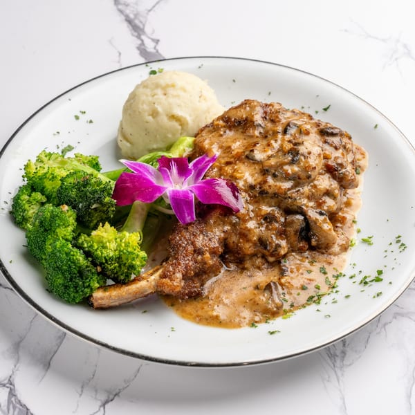 Italian pork chop with mushroom sauce, mashed potatoes, broccoli, and a purple orchid garnish.
