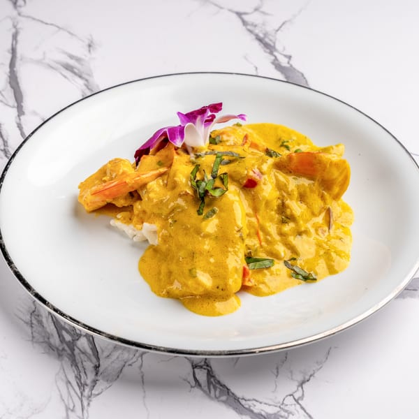 Shrimp and rice covered in a rich yellow curry sauce, garnished with basil and an orchid.