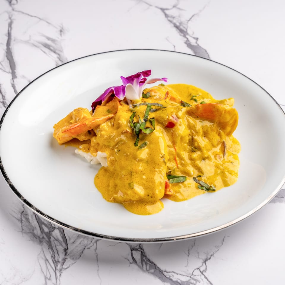 Shrimp and rice covered in a rich yellow curry sauce, garnished with basil and an orchid.
